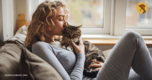 Woman kissing a tabby cat while sitting on a couch.